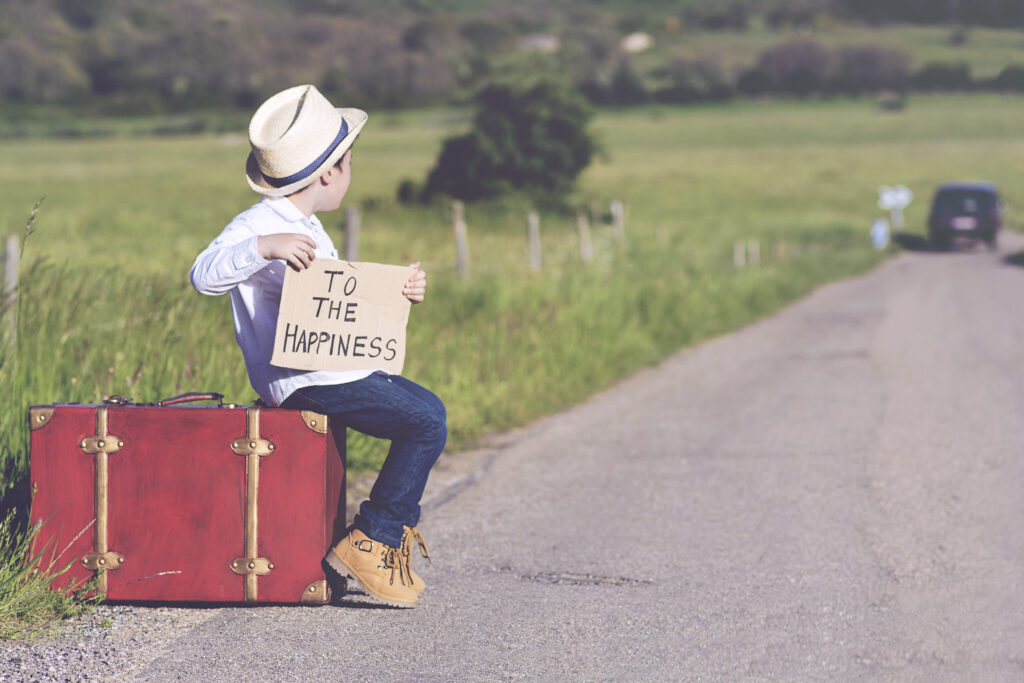 Boy sitting at the road side holding a sign that reads "To the happiness"