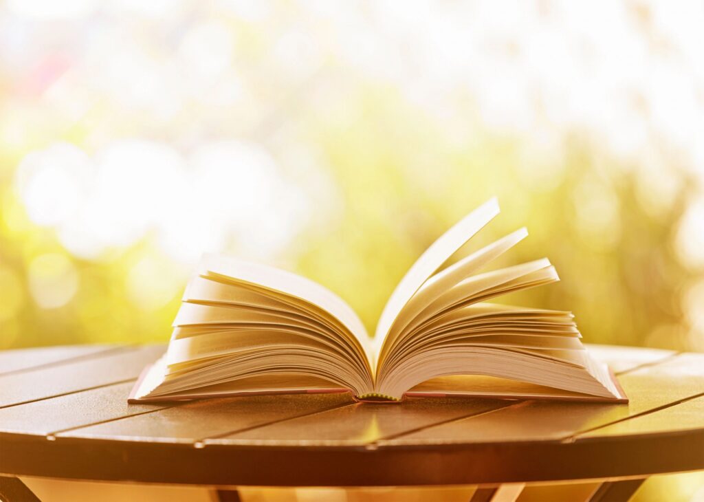 Open hardback book lying on garden table in soft sunshine